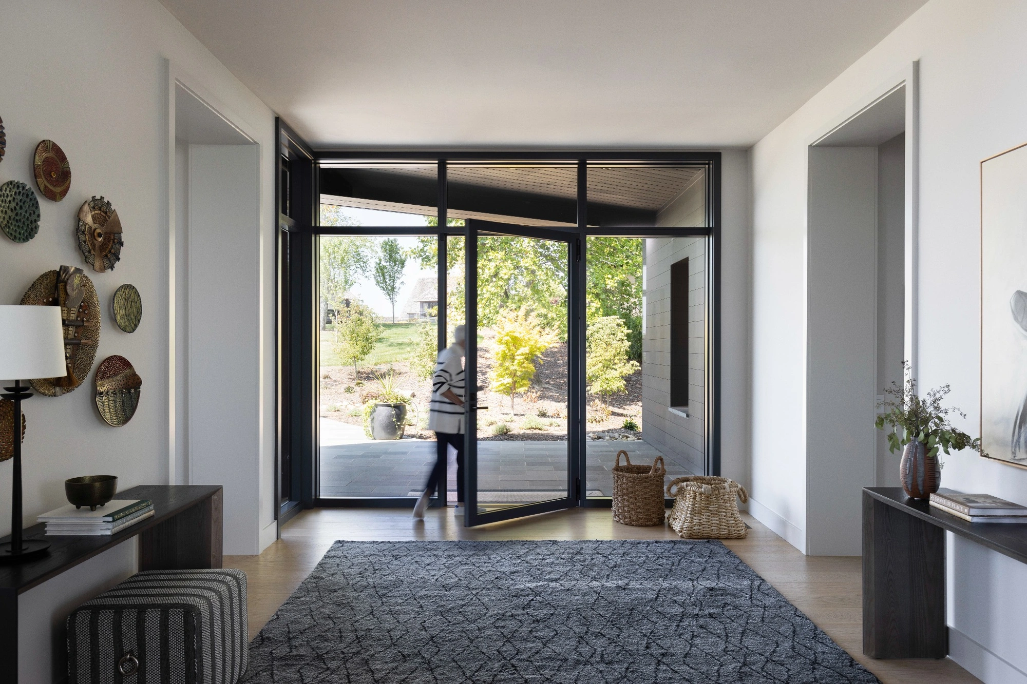 Bright modern entryway with large glass doors and black frames opening to a landscaped yard, illustrating how tall is a standard door frame in contemporary home design